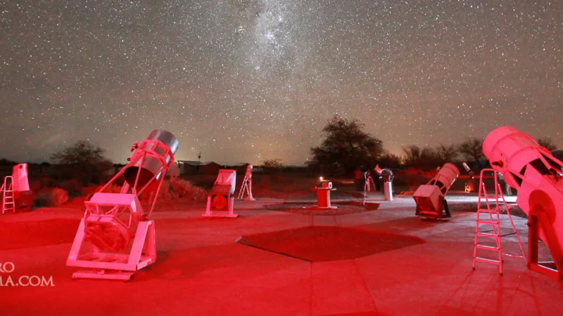 Observatorio en San Pedro de Atacama con telescopios iluminados en rojo bajo un cielo estrellado con la Vía Láctea visible.