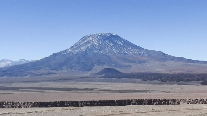 Snow-capped volcano rising above the arid Atacama Desert landscape under a clear blue sky