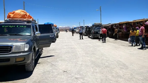 Veículos 4x4 estacionados em rua de terra no Mercado de Artesanías de Colchani, com barracas e turistas ao fundo